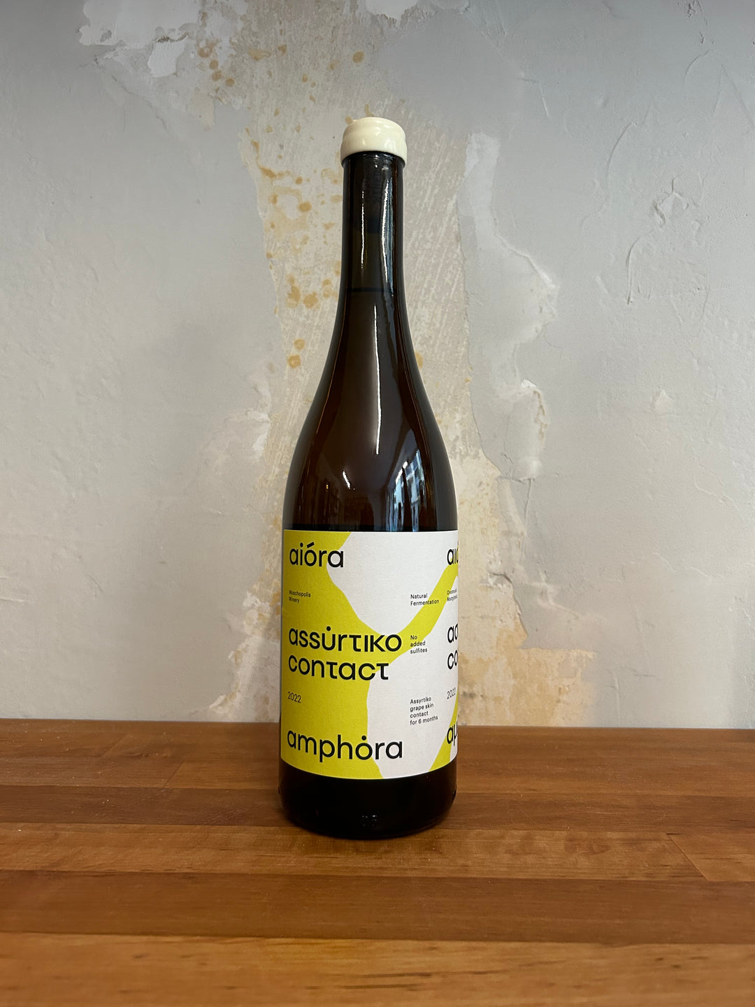 Flasche Moschopolis Winery Aiora Assyrtiko Amphora 2022. Die stilvolle Flasche zeigt ein ansprechendes Etikett mit eleganter Schrift und einem kreativen Design, das die Amphorenreifung und die einzigartigen Aromen des Assyrtiko-Weins hervorhebt.