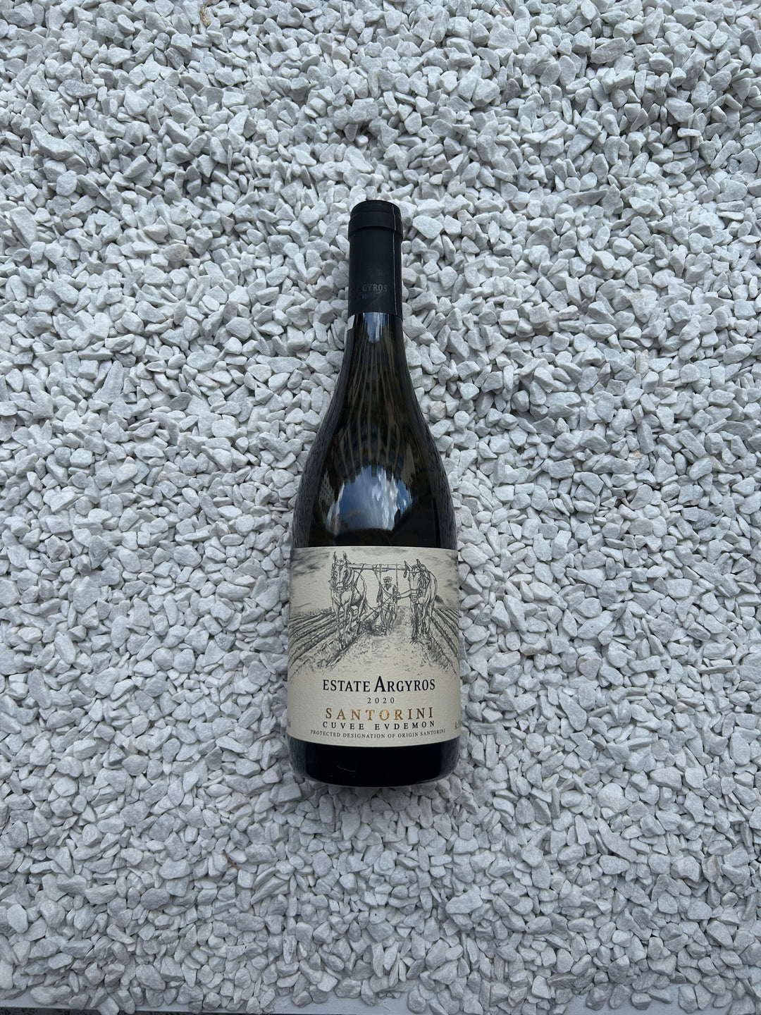 Flasche Argyros Estate Assyrtiko Cuvee Evdemon 2020. Die ansprechende Flasche ist mit einem eleganten Etikett versehen, das stilvolle Schriftzüge und ein Bild von Weintrauben zeigt, welches den charaktervollen und hochwertigen griechischen Weißwein hervorhebt.