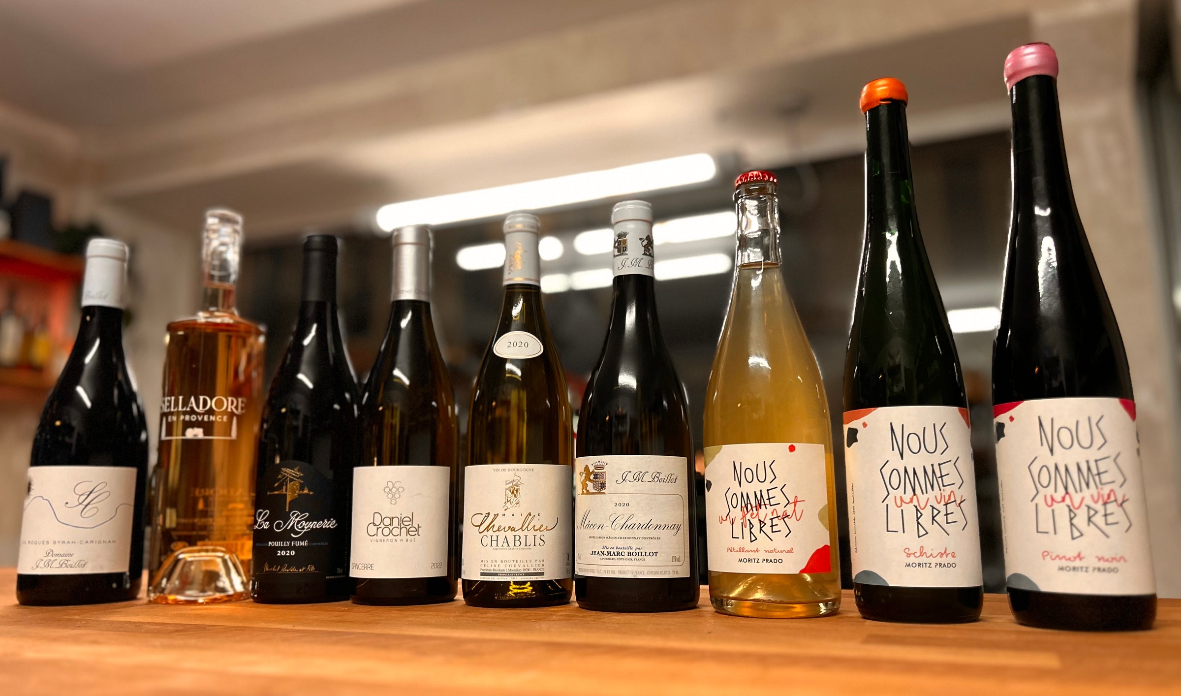 An assortment of nine French wines displayed on a rustic wooden table, featuring various bottle shapes, colors, and labels representing the diverse regions and flavors of French wine culture.